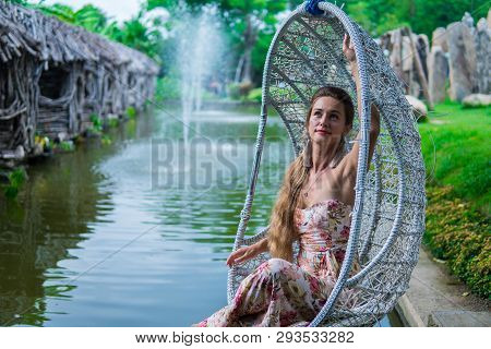 Beautiful Brunette In Dress Swinging On A Swing Over The Water In The Park In Sunny Day