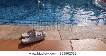 A Pair Of White Female Flip Flops Left Near Swimming Pool