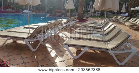 Rows Of Chaise Lounges For Tan And Rest Stay Empty On Stone Floor Near The Pool In Hotel Garden