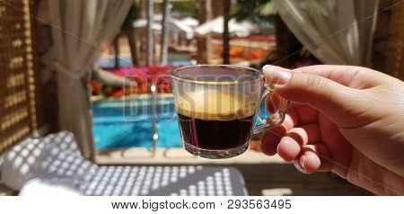 Cup With Black Coffee In Female Hand Against A View From Luxury Hotel Room On Outside Pool Surrounde