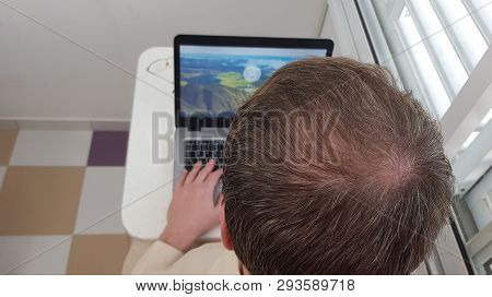 Male Head With Blond Hair Starting To Gray Over Open Laptop Computer Standing On White Table In Smal