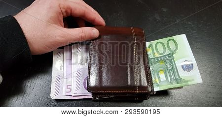Male Hand Touch A Brown Leather Wallet Full With Euro Banknotes Laying On Black Table