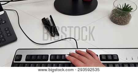 Female Hand On Black Computer Keyboard Near Office Phone Stepler And Small Green Plant In Transparen