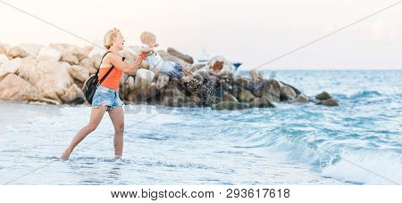 Woman Playing With Her Baby Outside Against The Sea. The Concept Of A Happy Full-fledged Family Life