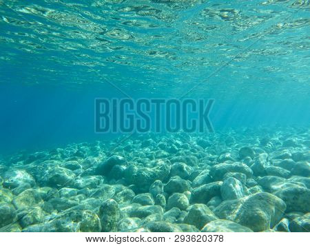 Underwater View Of Turquoise Clear Water And White Pebbles Scattered Off The Seabed Of The Antisamos