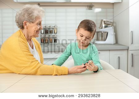 Senior Woman With Her Grandson Using Digital Glucometer At Home. Diabetes Control