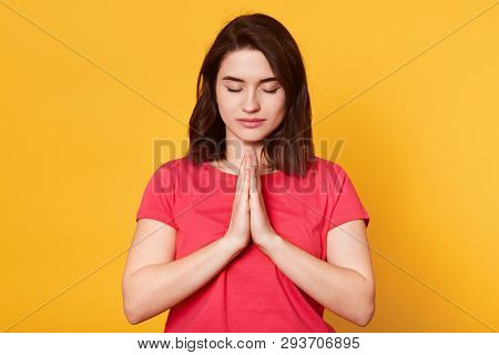 Beautiful Young Brunette Female Makes Praying Gesture, Keeps Palms Pressed Together, Feels Guilty, D