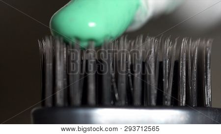 Extreme Close Up Of A Grey Toothbrush With Green Toothpaste Being Squeezed From The Tube On Dark Gre