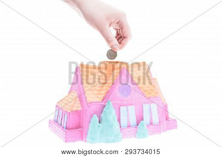 Hand Drops A Coin Into The Piggy Bank House On A White Background, Shallow Depth Of Field
