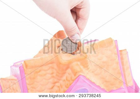 Hand Drops A Coin Into The Piggy Bank House On A White Background, Shallow Depth Of Field