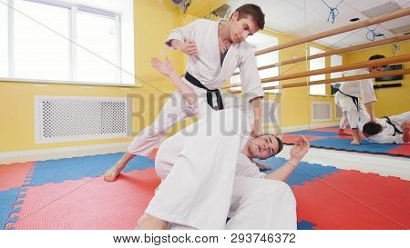 Two Men Training Their Aikido Skills In The Studio. A Man Lying On The Floor And Protecting From The