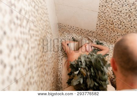 Slim Woman In Bath Is Getting Steaming Massage With Hot Oak Leaves Brooms, In Steam-room