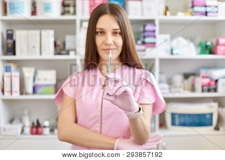 Doctor In Pink Gown And Gloves Holds Syringe In Medical Office, Ready For Making Injections. Cosmeto