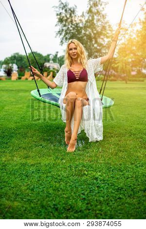 Youmg Beautiful Woman In Beautiful Summer Garden Is Round Swing