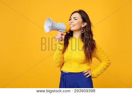 Smiling Young Woman In Sweater, Blue Trousers Looking Aside, Scream In Megaphone Isolated On Yellow 