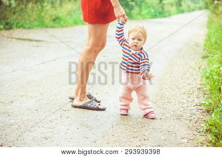 The Child Learns To Walk In The Park Barefoot On The Grass