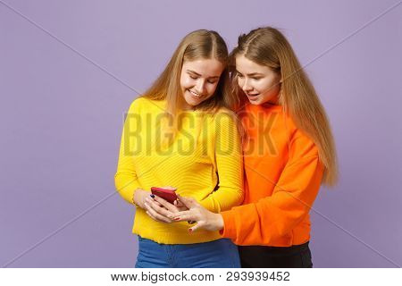 Two Smiling Amazed Young Blonde Twins Sisters Girls In Vivid Clothes Using Mobile Phone Typing Sms M