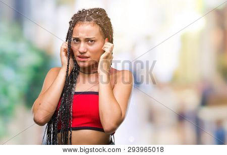 Young braided hair african american with pigmentation blemish birth mark over isolated background covering ears with fingers with annoyed expression for the noise of loud music. Deaf concept.
