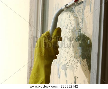 Process of window washing. A hand in rubber glove cleaning window by special cleaning brush, squeegee. Window is covered with a cleaner foam