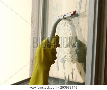 Process of window washing. A hand in rubber glove cleaning window by special cleaning brush, squeegee. Window is covered with a cleaner foam