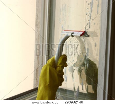 Process of window washing. A hand in rubber glove cleaning window by special cleaning brush, squeegee. Window is covered with a cleaner foam