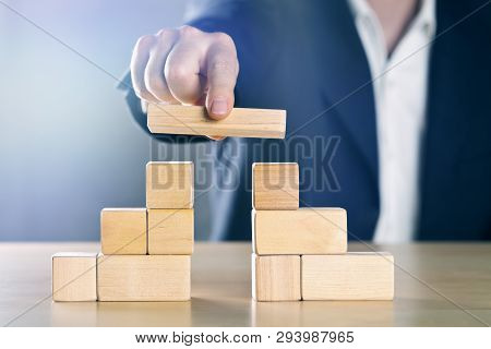 Business Man Bridging The Gap Between Two Towers Or Parties Made From Wooden Blocks; Conflict Manage