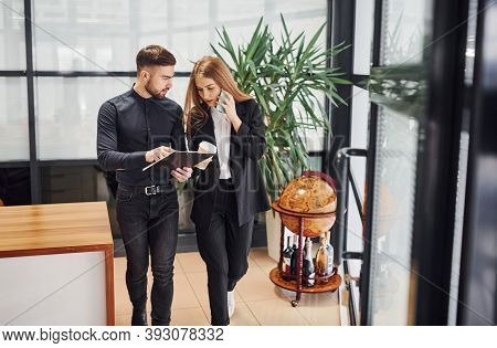 Woman And Man In Formal Clothes With Documents Talking To Each Other In The Office.