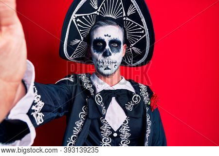 Young man wearing mexican day of the dead costume make selfie by the camera thinking attitude and sober expression looking self confident 
