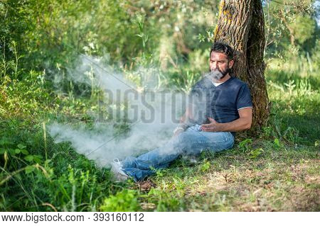 Confident Vaper Exhaling Vapor From Electronic Cigarette In The Daylight. Man Really Likes Process O