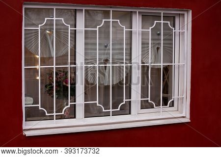 There Is A Fragment Of The Facade Of An Old House, Including A Window With Bars. A Window With A Cur