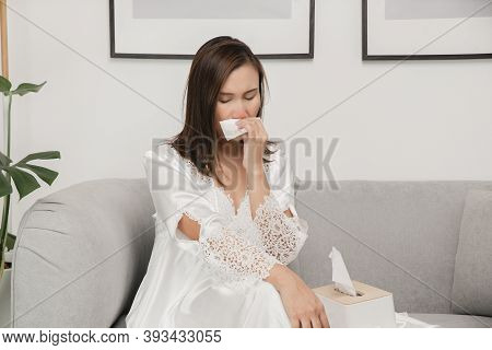 Symptoms Of Allergic Rhinitis In Women. Sick Woman In White Nightwear With A Cold Blowing Her Nose I