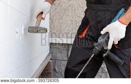 Insulation Of The House With Polyfoam. A Worker Is Using A Hammer For Dowels That Fasten Polystyrene