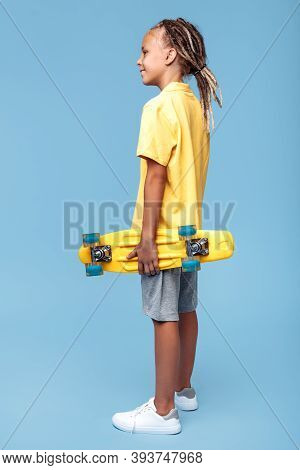 Trendy Little Boy With African Dreads With Skateboard On The Blue Background. Back View.