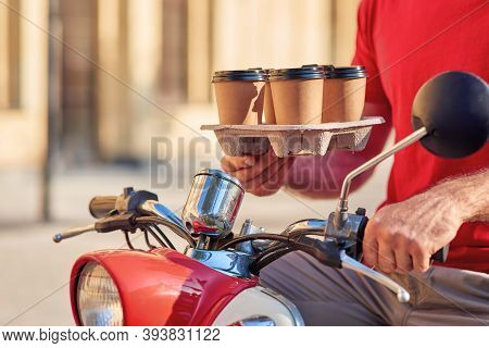 Male Courier Delivering Four Coffee Cups On Scooter, Standing On A Sunny Street