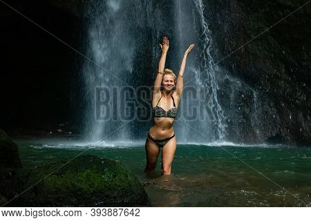 Young Caucasian Woman With Blond Hair Standing Near The Waterfall. Happy Smiling Woman Wearing Bikin