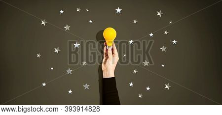 Person Holding A Yellow Light Bulb With Silver Shiny Stars