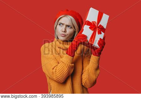 Adorable Caucasian Woman With Blonde Hair And Red Hat With Gloves Is Shaking A Present Box Guessing 