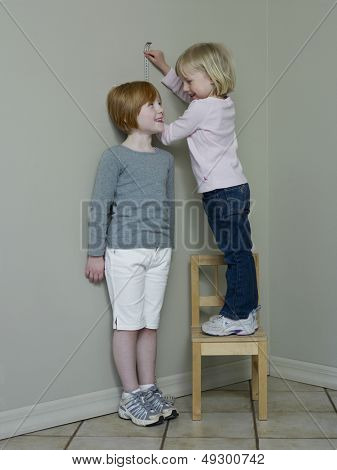 Full length of two girls measuring height against wall