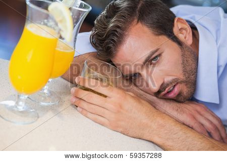 Drunk businessman slumped on bar beside cocktail at the local bar