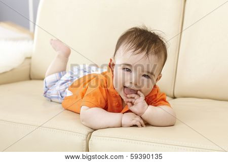 Beautiful baby boy lying on sofa, smiling happy with hand in mouth.