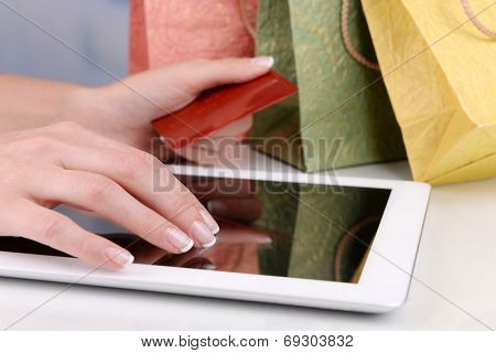 Female hands holding credit card with computer tablet and paper bags on table close up