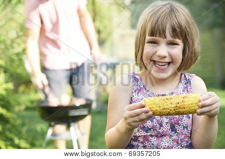 Young Girl Eating Sweetcorn At Family Barbeque