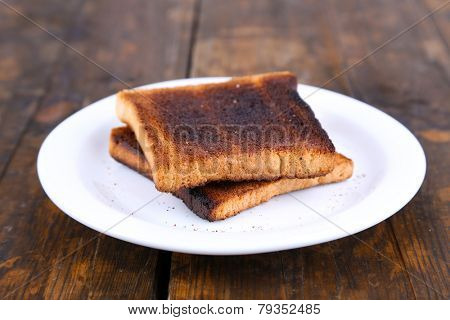 Burnt toast bread on plate, on wooden table background