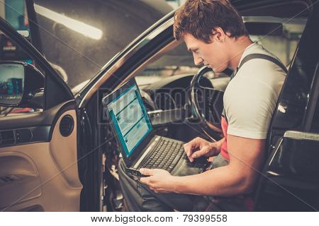 Serviceman making car diagnostics with laptop in a workshop