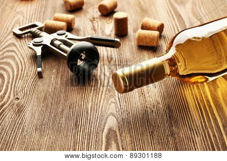 Glass bottle of wine with corks and corkscrew on wooden table background