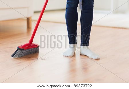 people, housework, cleaning and housekeeping concept - close up of woman legs with broom sweeping floor at home