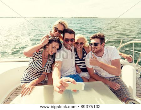 vacation, travel, sea, friendship and people concept - smiling friends sitting on yacht deck and making selfie
