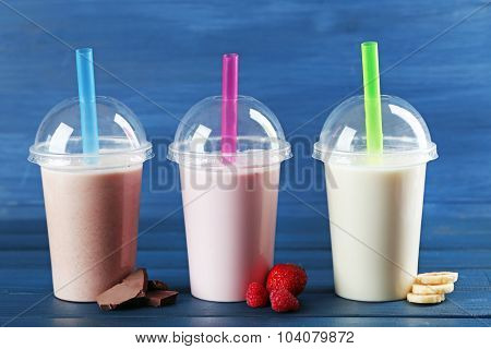 Plastic cups of milkshake on color wooden background
