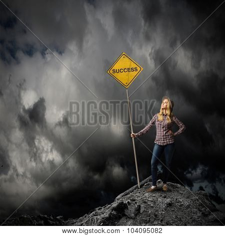 Young woman satnding on rock top with signboard