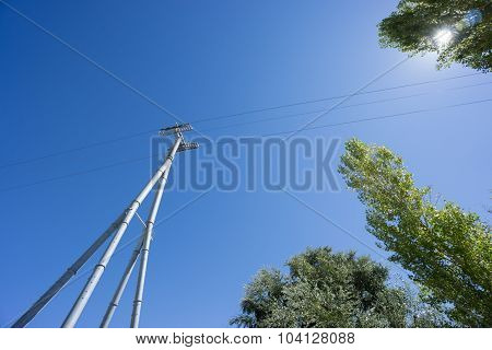 Railway catenary against a blue sky and sun